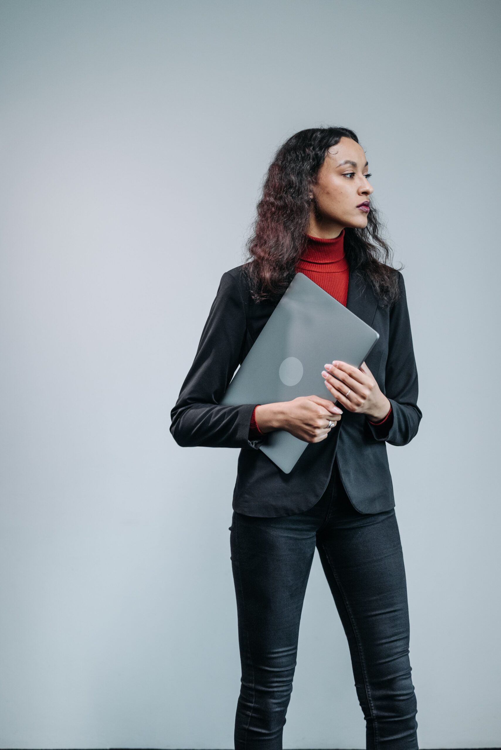 Confident businesswoman in a studio setting, holding a laptop against a light grey background.
